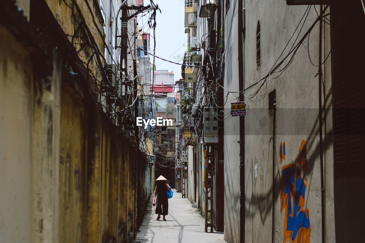 Woman walking amidst buildings at alley in city