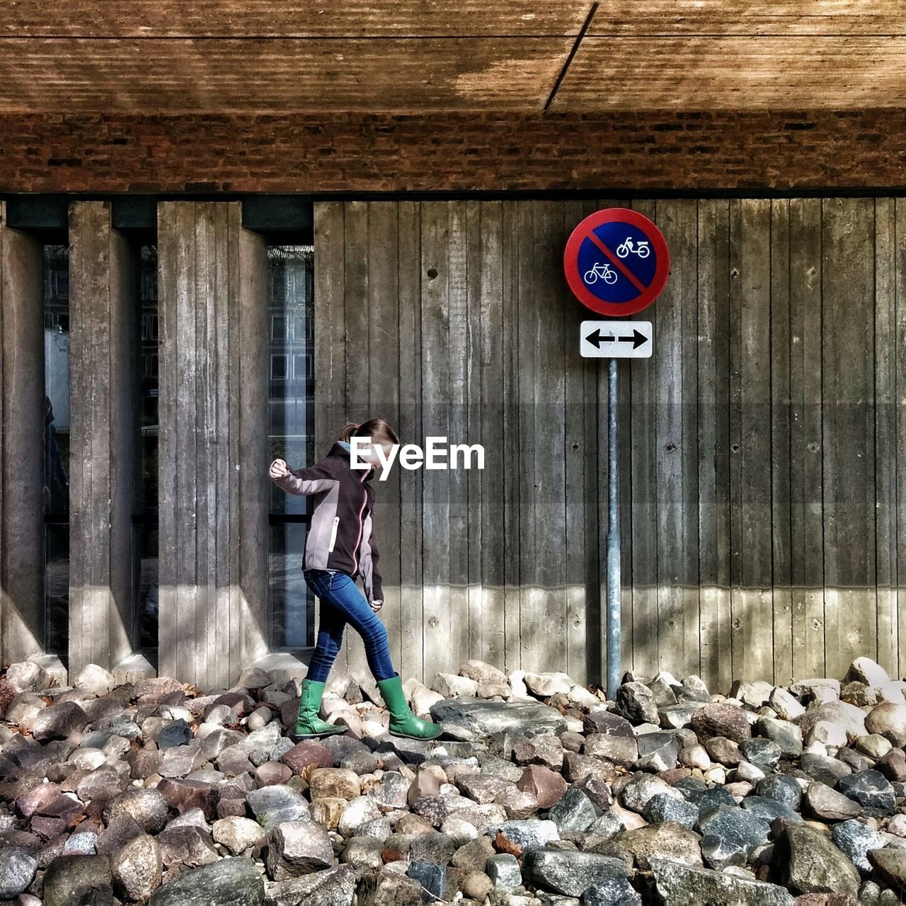 Full length of girl walking on stones by road sign against wooden wall