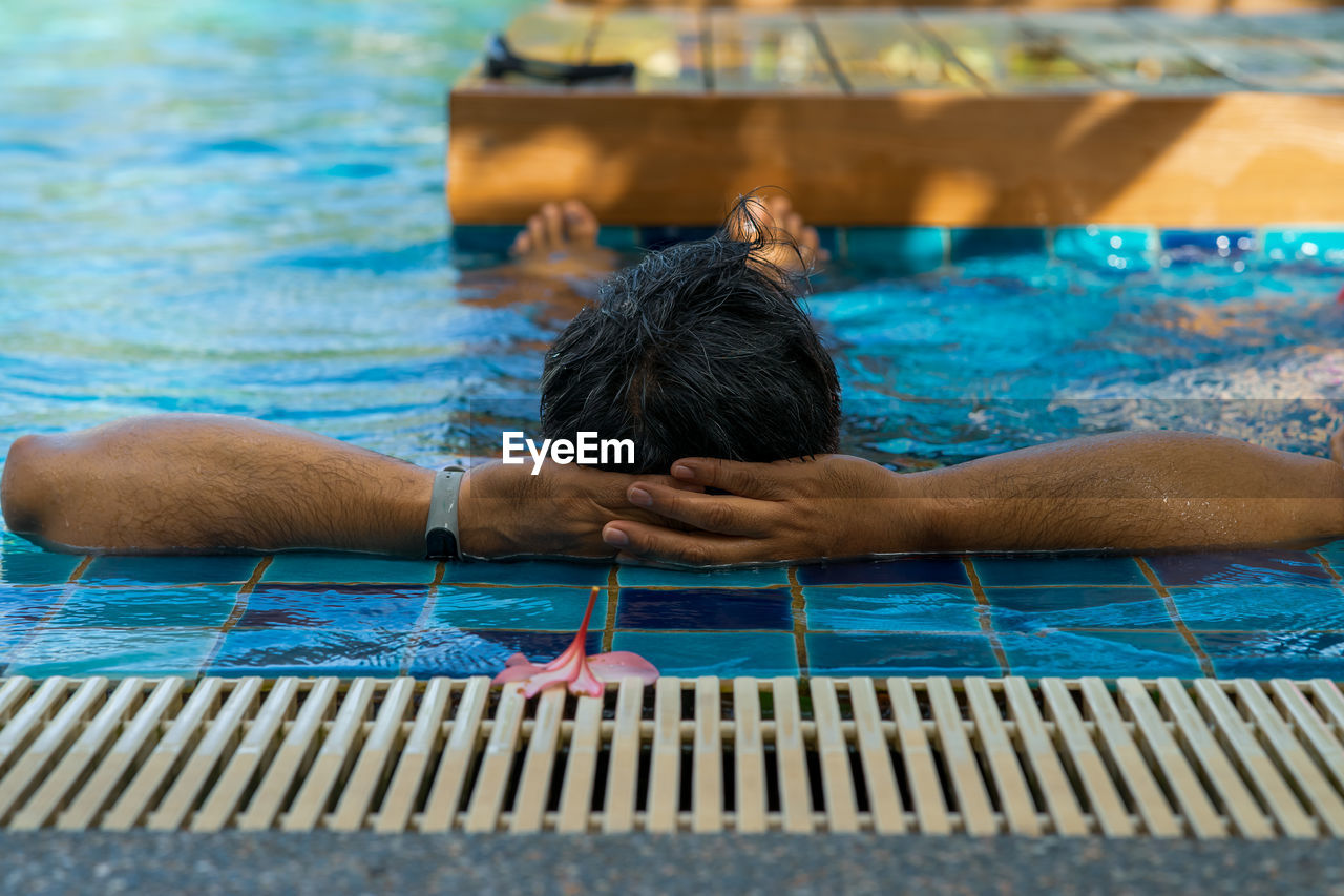 Back view of a tanned colour man relaxing in the swimming pool. summer vacation