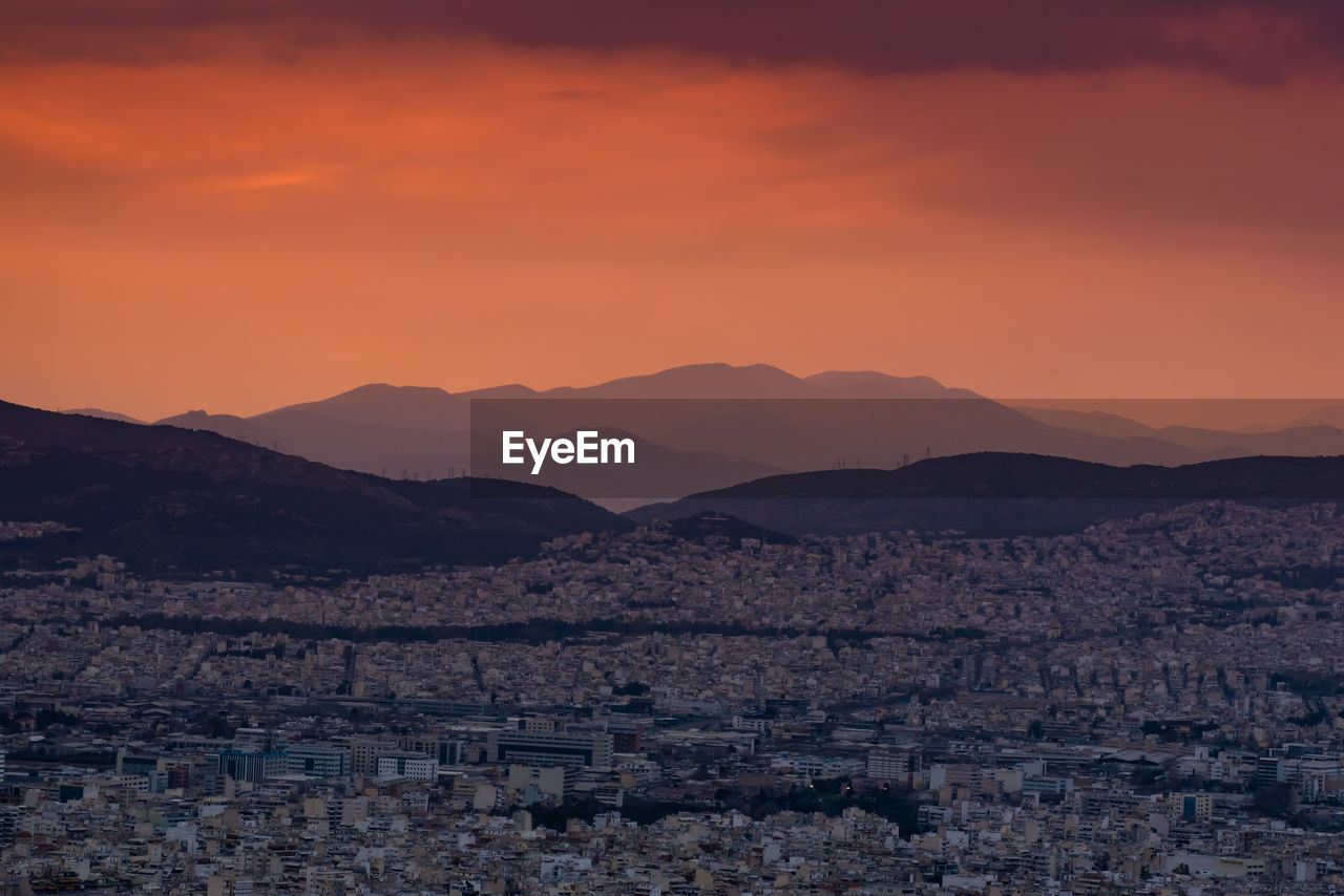 SCENIC VIEW OF TOWN AND MOUNTAINS AGAINST SKY DURING SUNSET