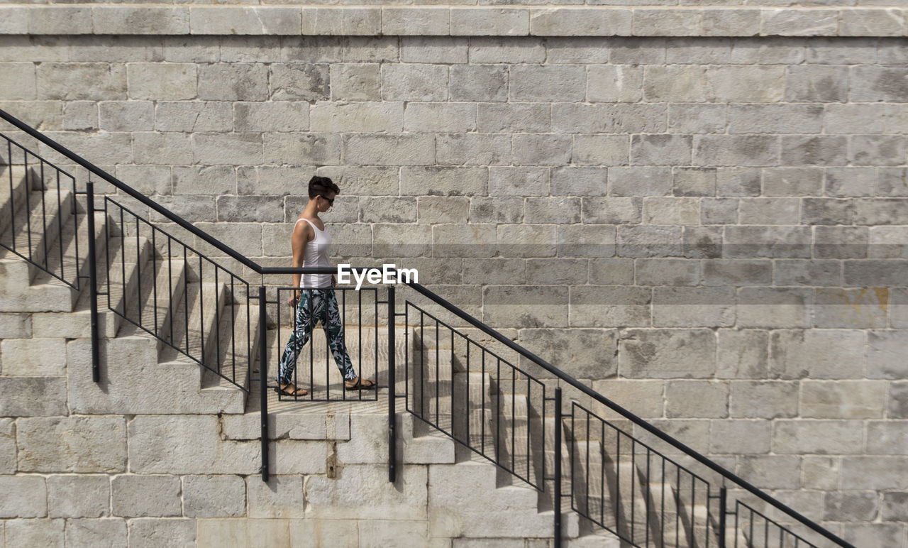 Woman walking on staircase by brick wall