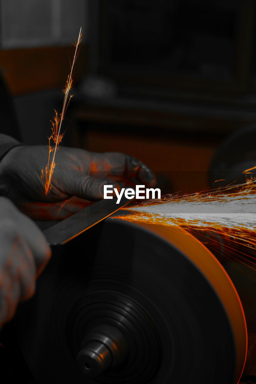 Worker sharpening knife on wheel in dark at workshop