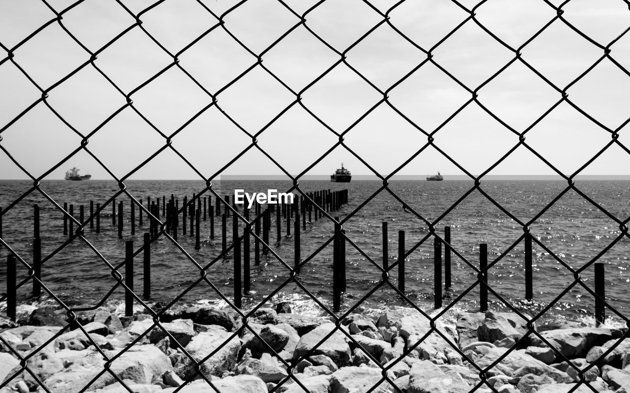 Wooden posts in sea seen through chainlink fence