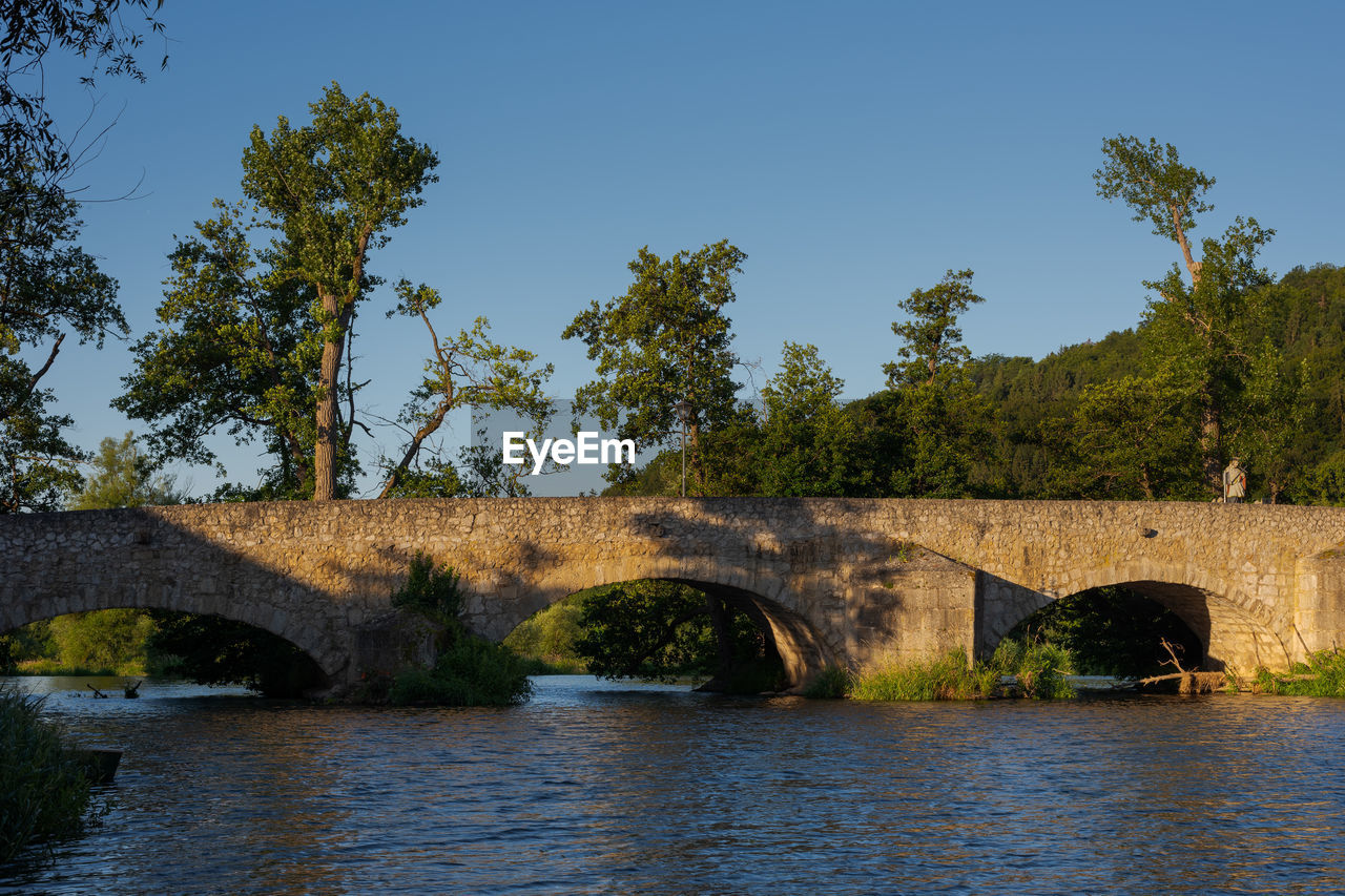 ARCH BRIDGE OVER RIVER AGAINST TREES