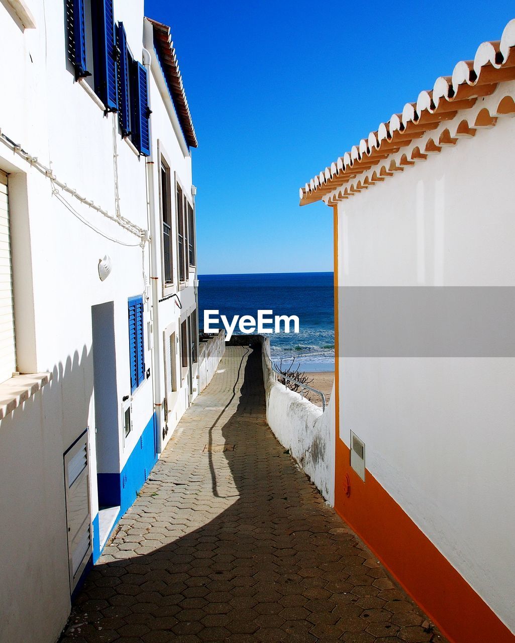 Footpath amidst buildings by sea against sky