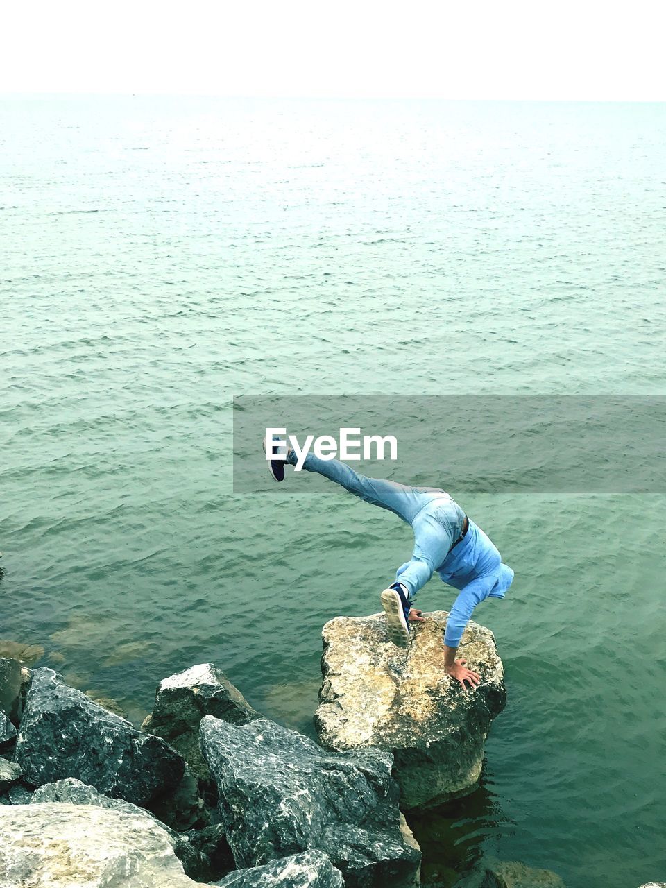 Man doing handstand on rock by sea