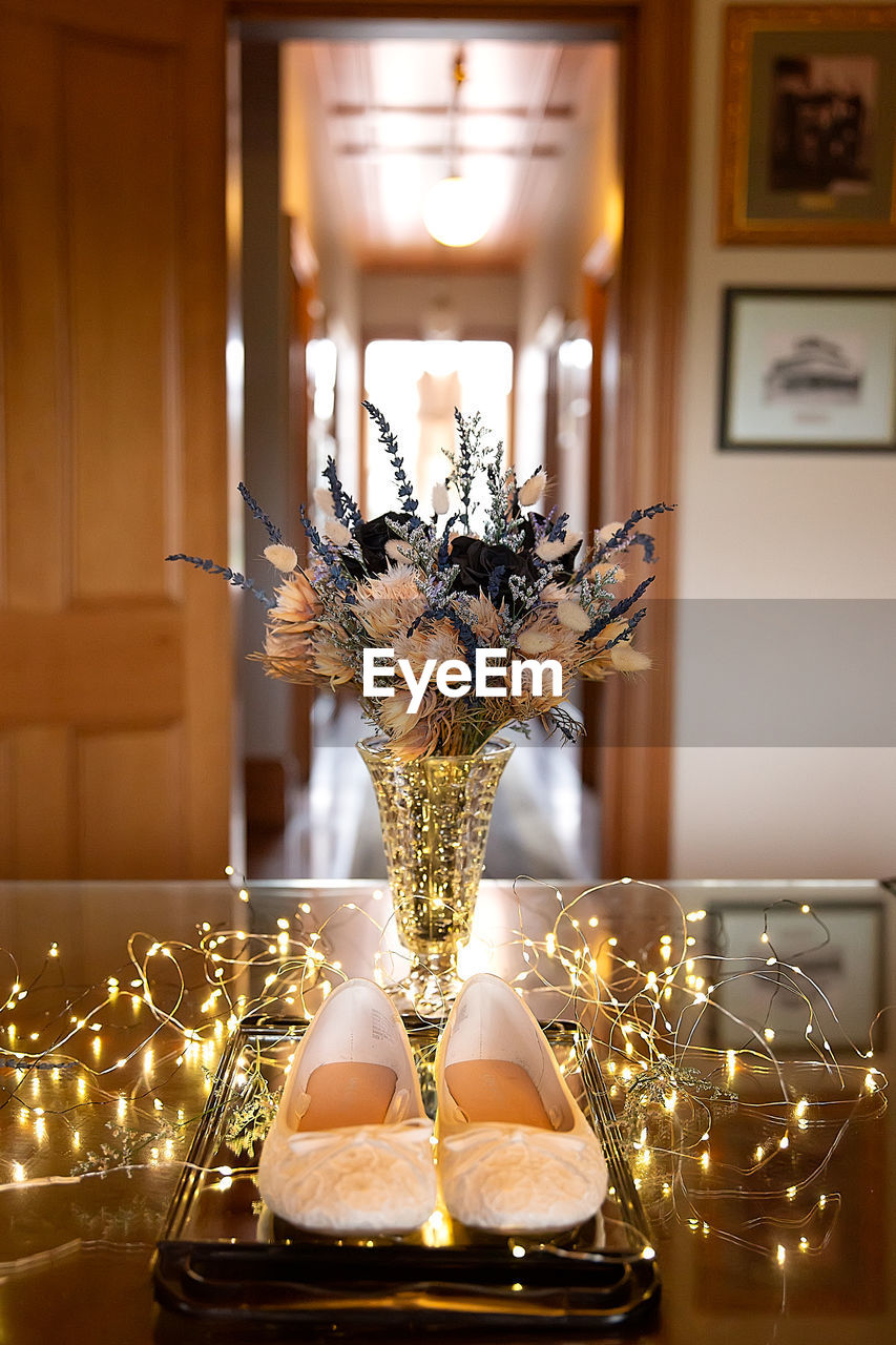 Dried flowers in vase with fairy lights and wedding shoes in historic building backlit window hall