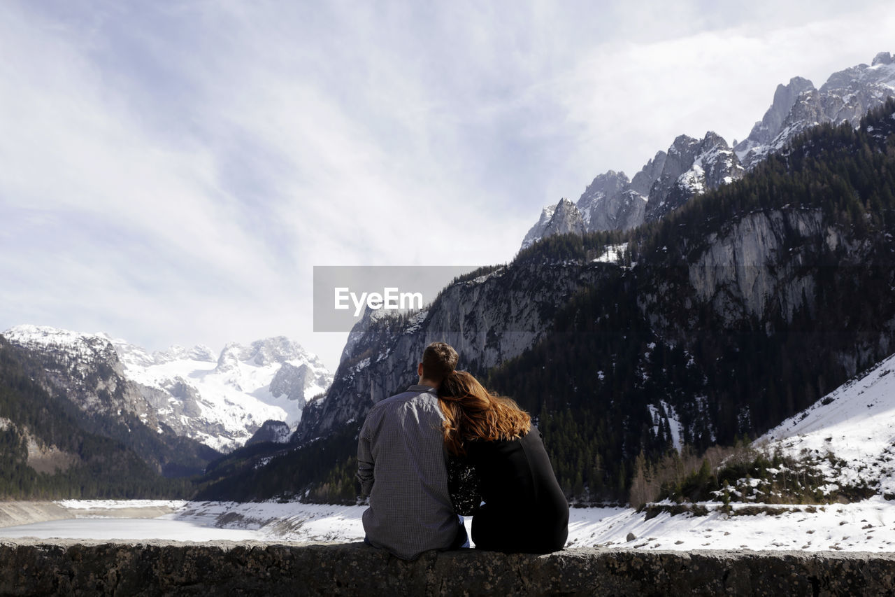 REAR VIEW OF WOMAN ON SNOWCAPPED MOUNTAIN AGAINST SKY