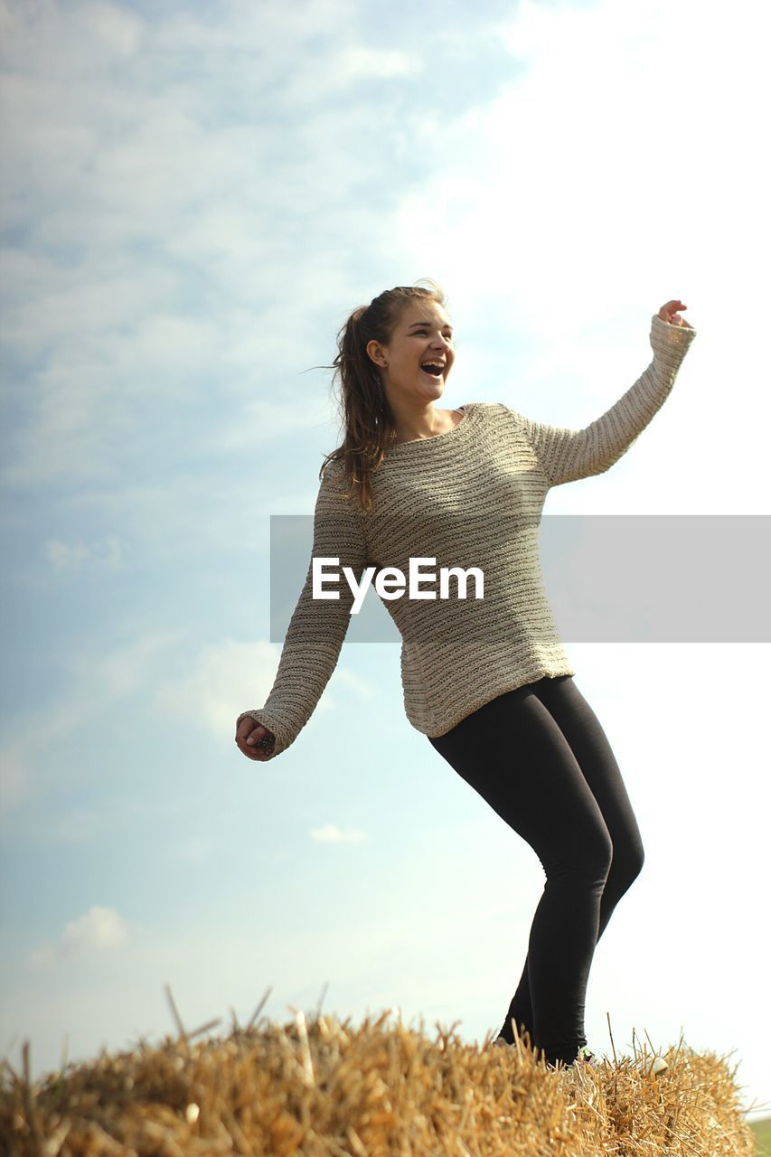 Low angle view of happy young woman on haystack against sky