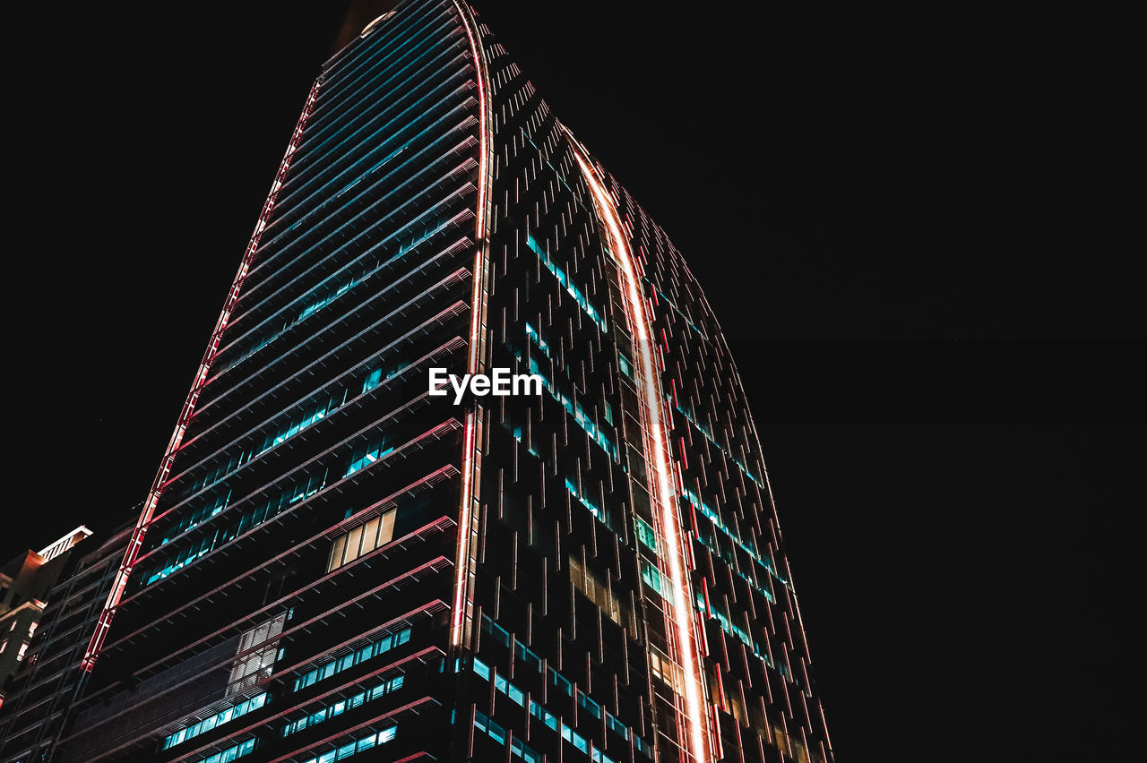 LOW ANGLE VIEW OF ILLUMINATED MODERN BUILDING AGAINST SKY AT NIGHT