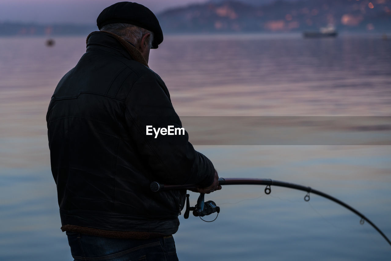 MIDSECTION OF MAN FISHING AT SEA