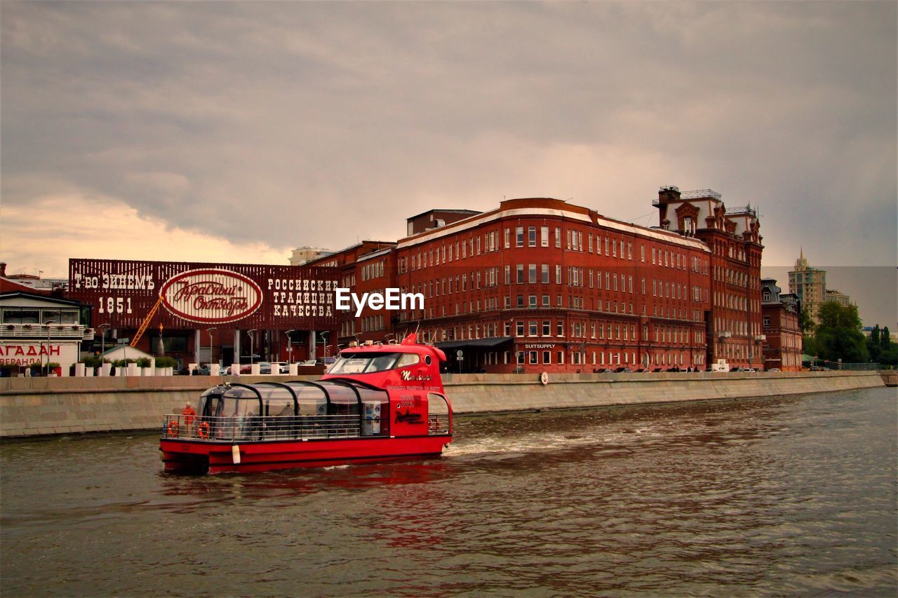 RED BOAT IN RIVER AGAINST BUILDINGS IN CITY