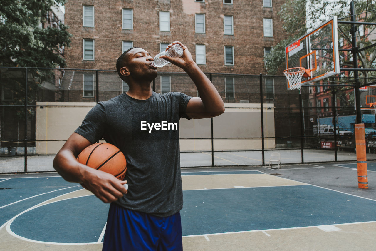 Male athlete holding basketball while drinking water in court