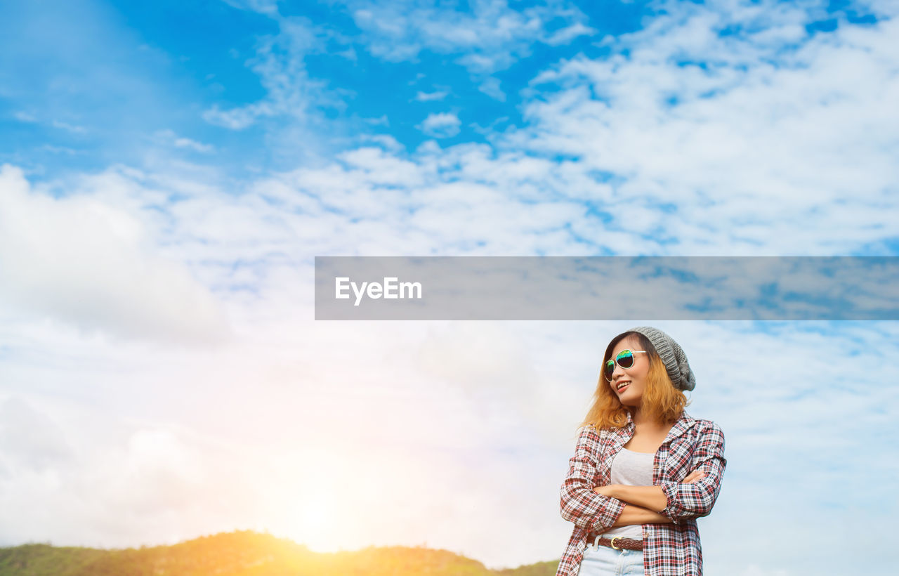 Smiling young woman standing against sky