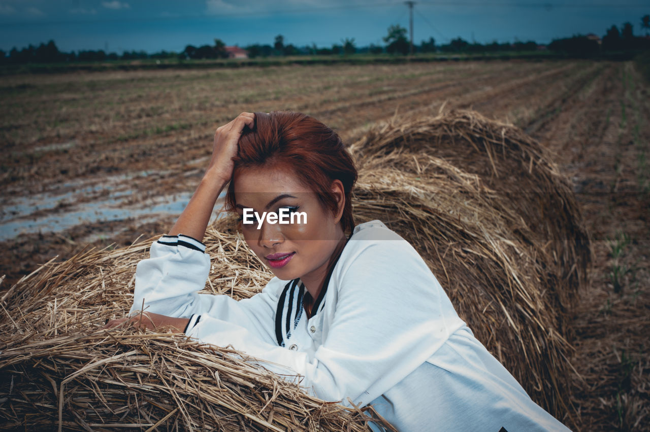 Portrait of woman sitting on hay bale at field