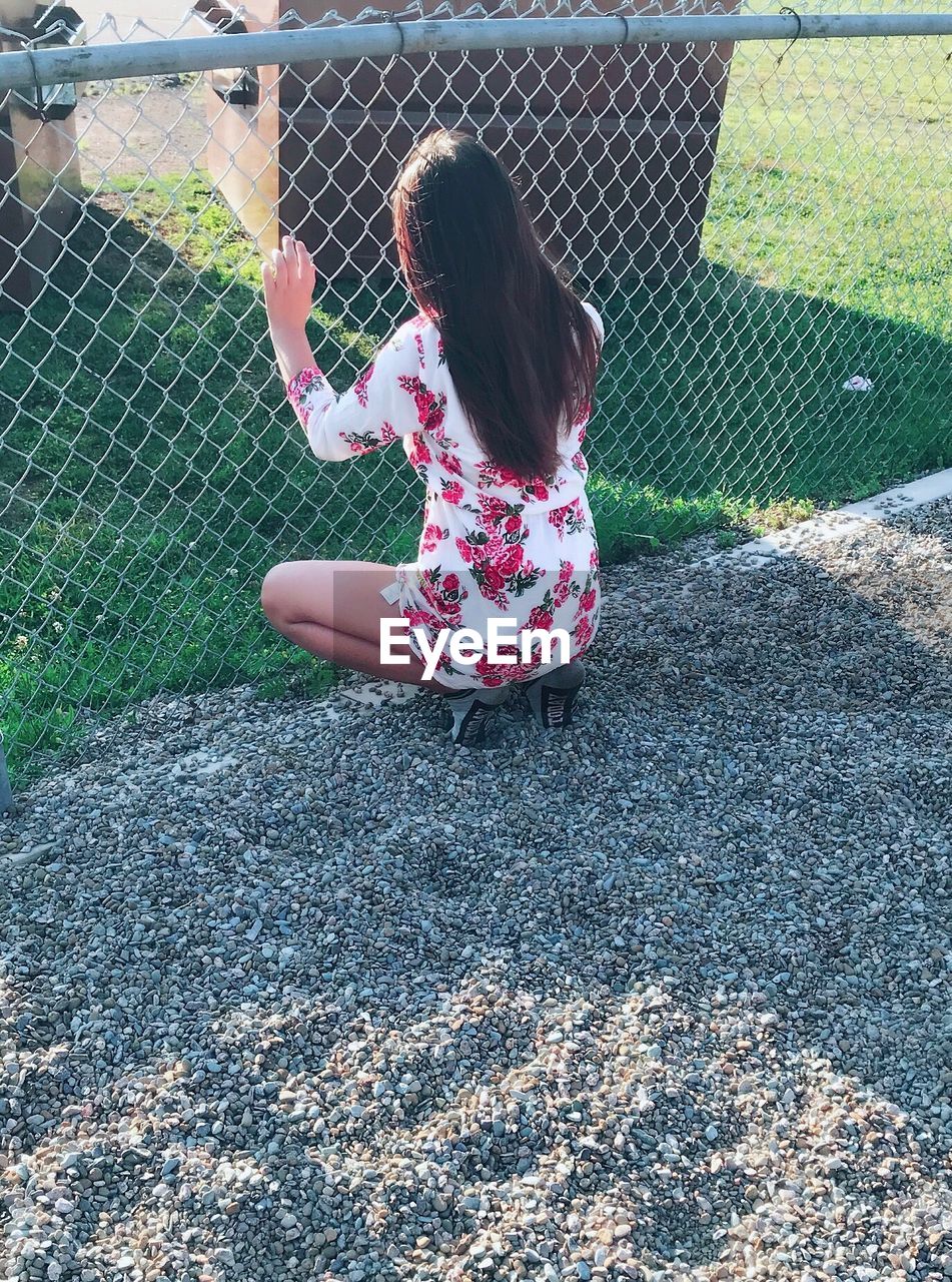 Teenage girl crouching by chainlink fence