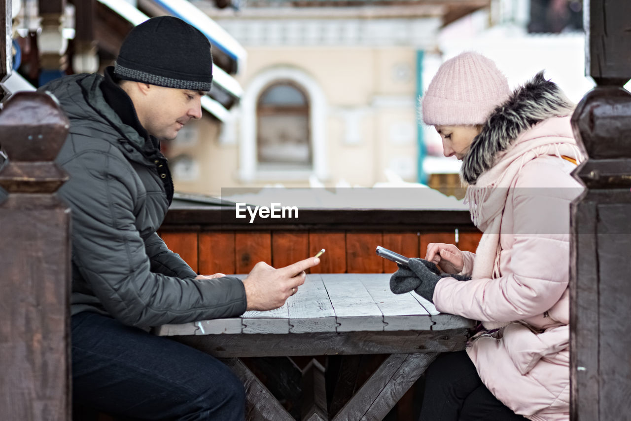 A couple is waiting for their order for lunch in a street cafe, texting by phone. communication