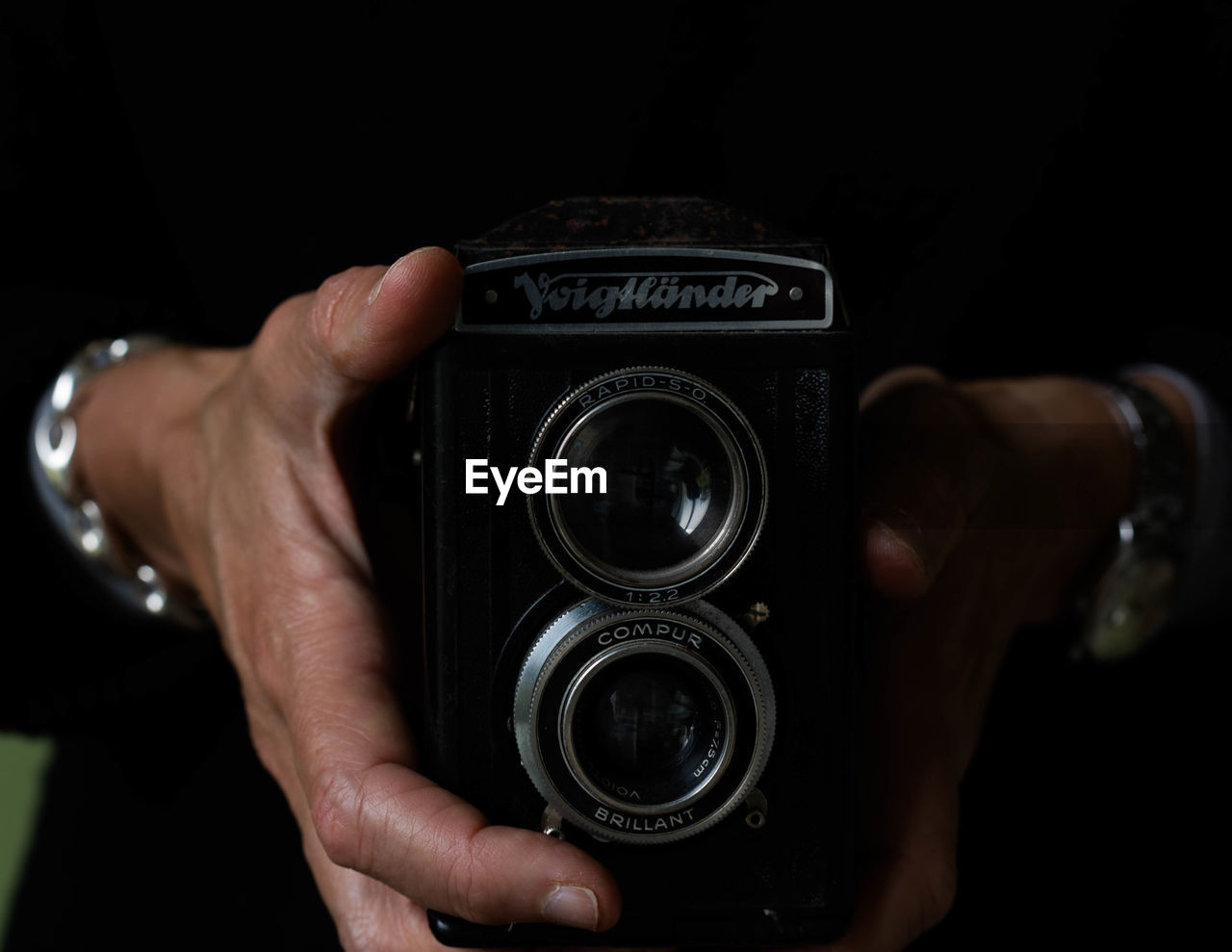 camera, hand, technology, one person, holding, photographing, lens - optical instrument, adult, activity, close-up, indoors, photographic equipment, photographer, digital slr, black background, occupation, lens - eye, black, men, retro styled, focus on foreground, studio shot