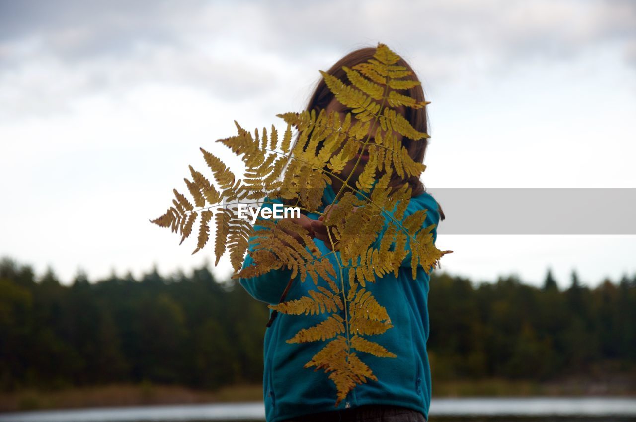 Girl holding standing with leaves against sky