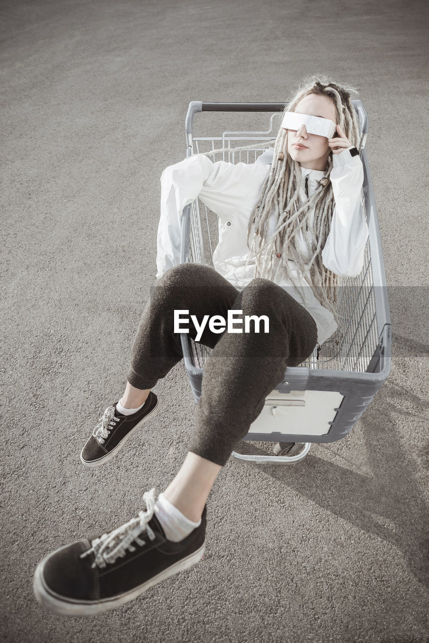 High angle view of young woman with dreadlocks sitting in shopping cart