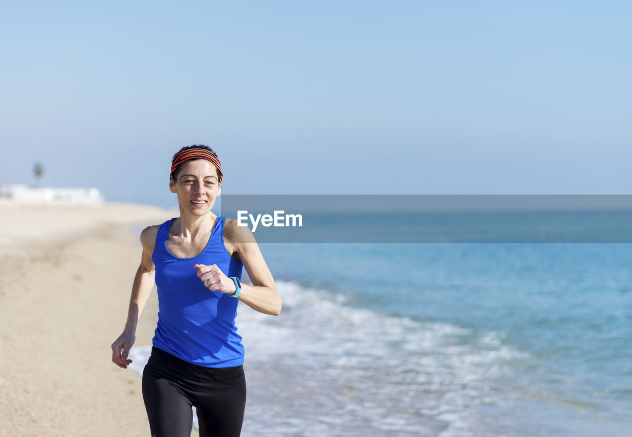 Woman running at beach against clear blue sky