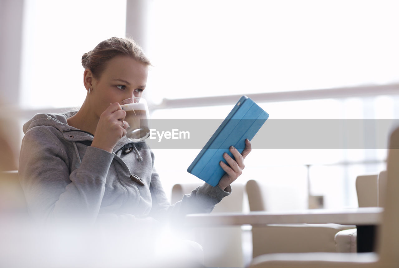 Woman drinking coffee while holding digital tablet