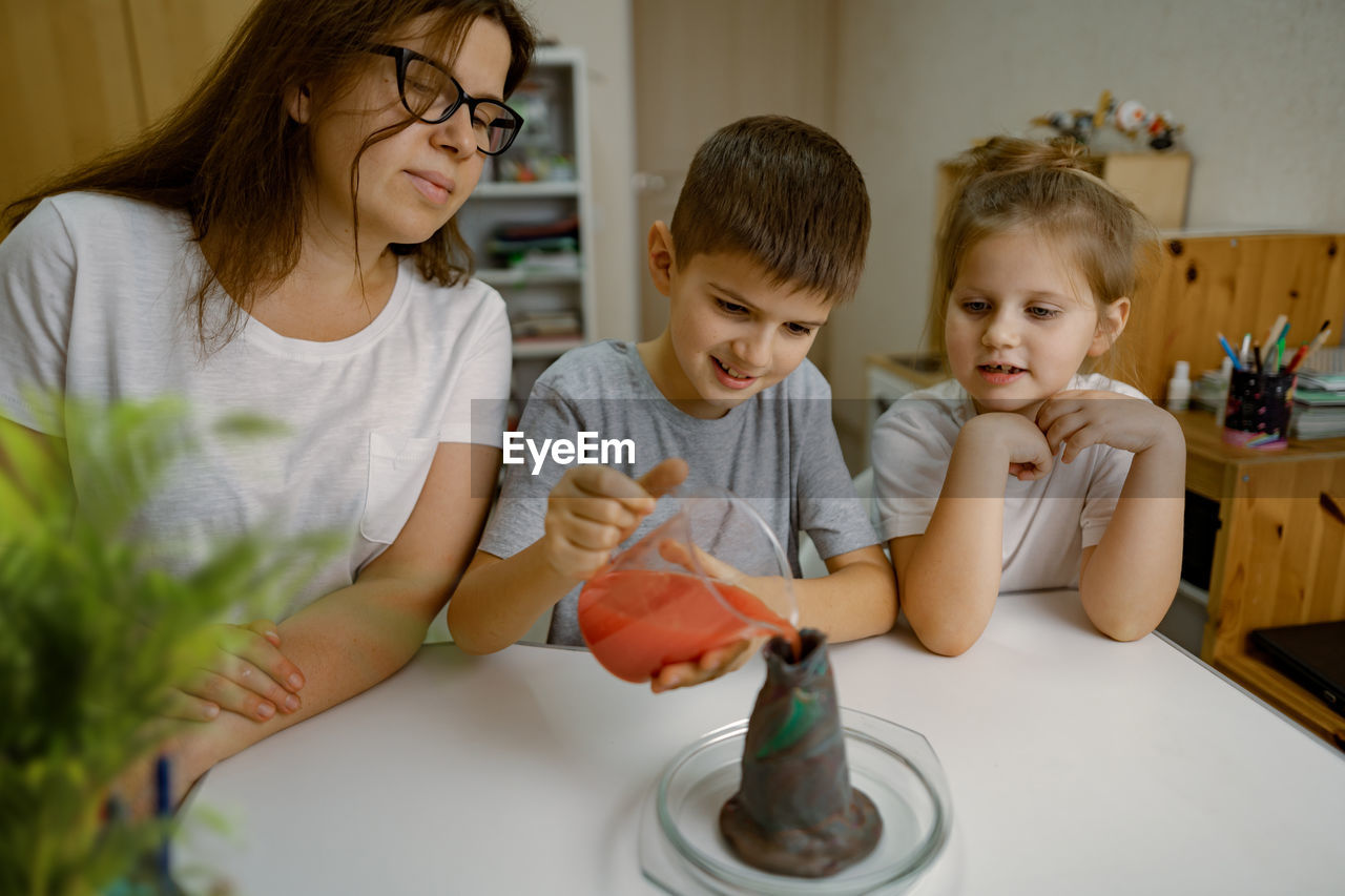 Mom and children at home are conducting an experiment with a volcanic eruption.