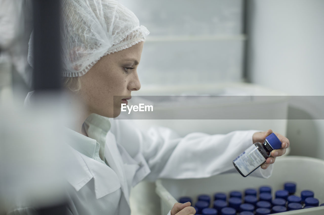 Lab worker in pharmaceutical plant looking at pill bottle