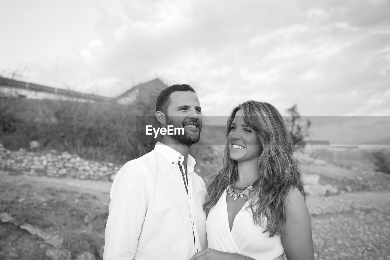 Smiling young couple looking away while standing on land