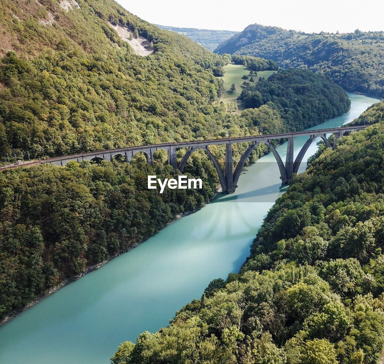 HIGH ANGLE VIEW OF ARCH BRIDGE OVER RIVER AGAINST MOUNTAINS