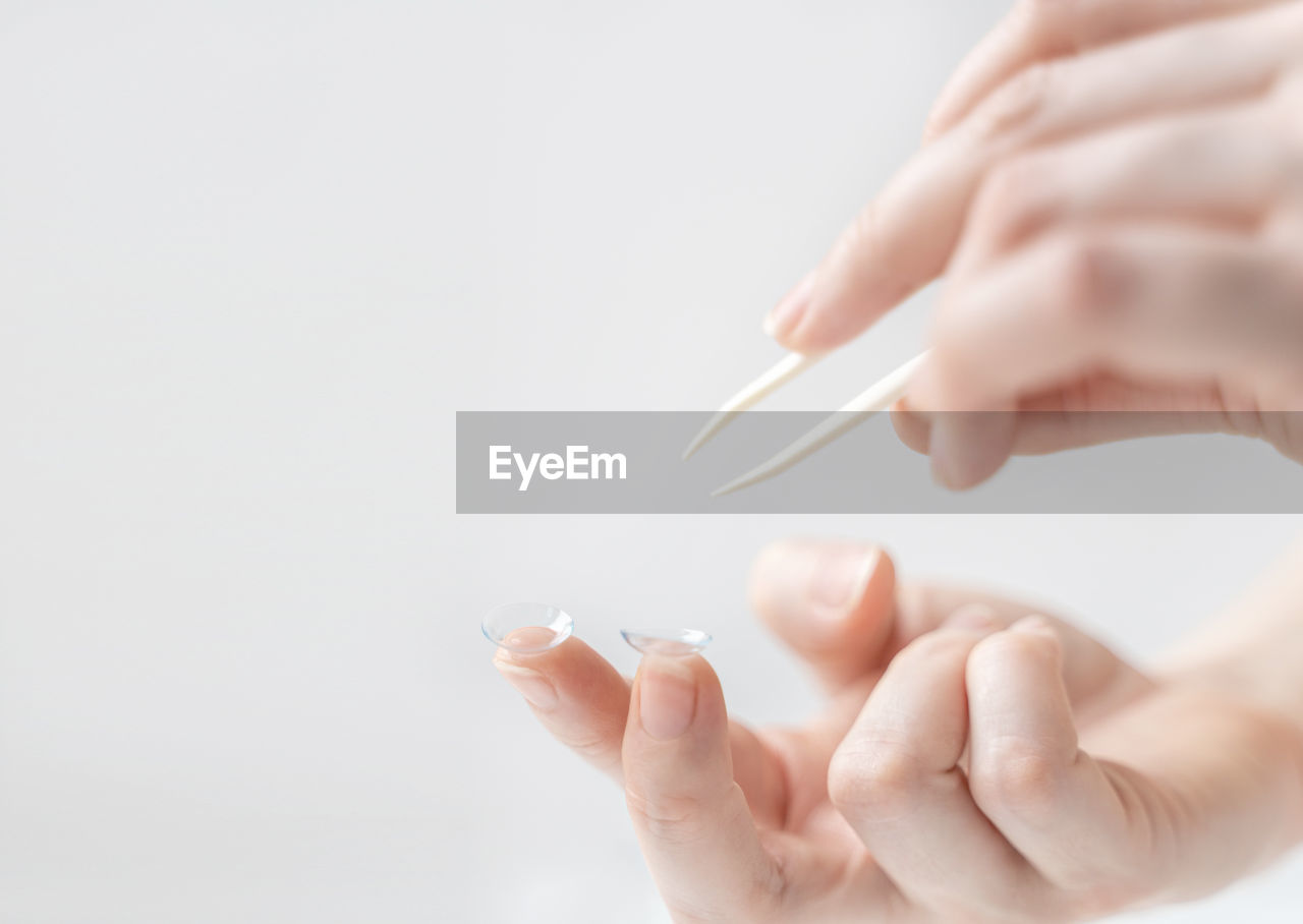 Close-up of woman holding hands with contact lenses over white background