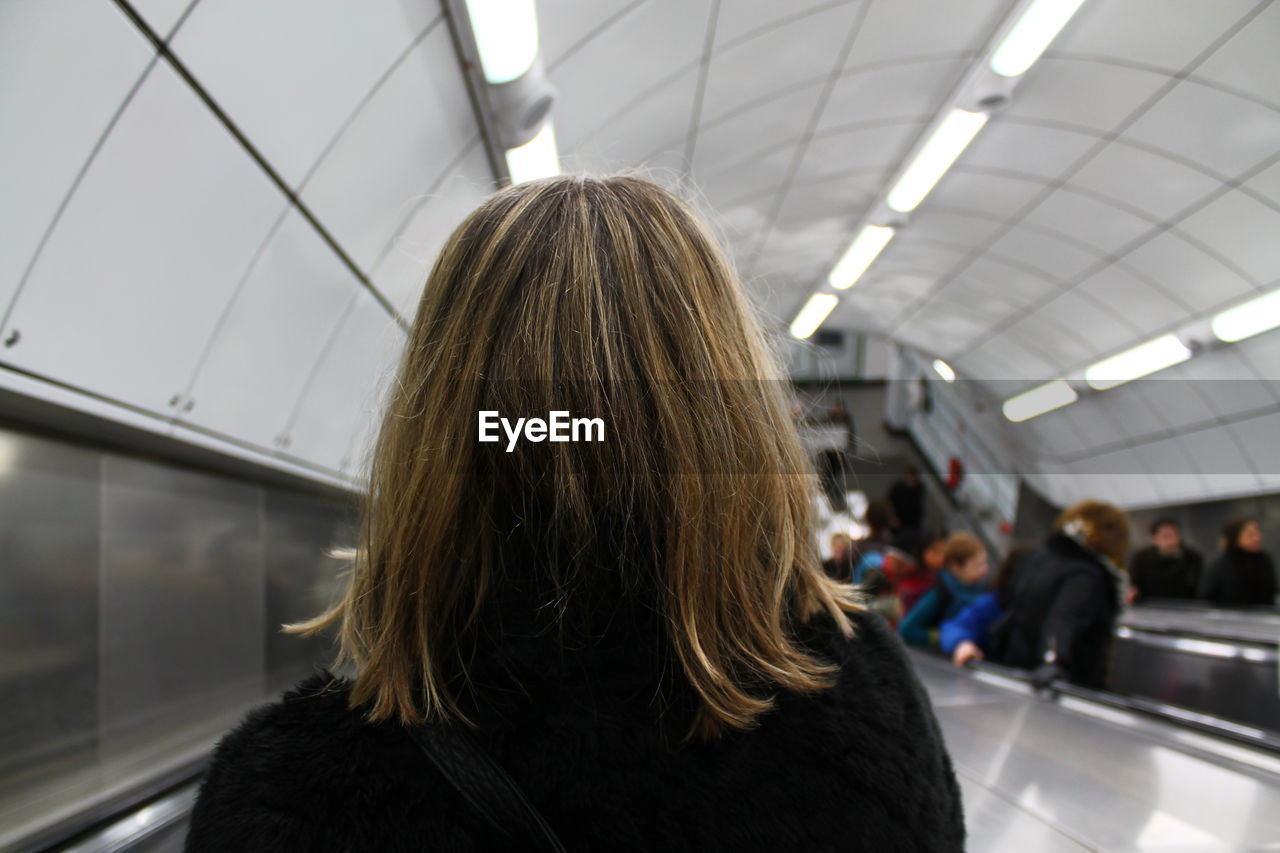 Rear view of woman standing on escalator at illuminated subway station