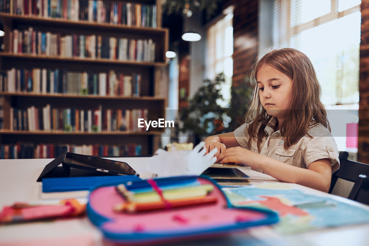 Girl doing homework, learning, drawing pictures, doing puzzles in school library. primary school