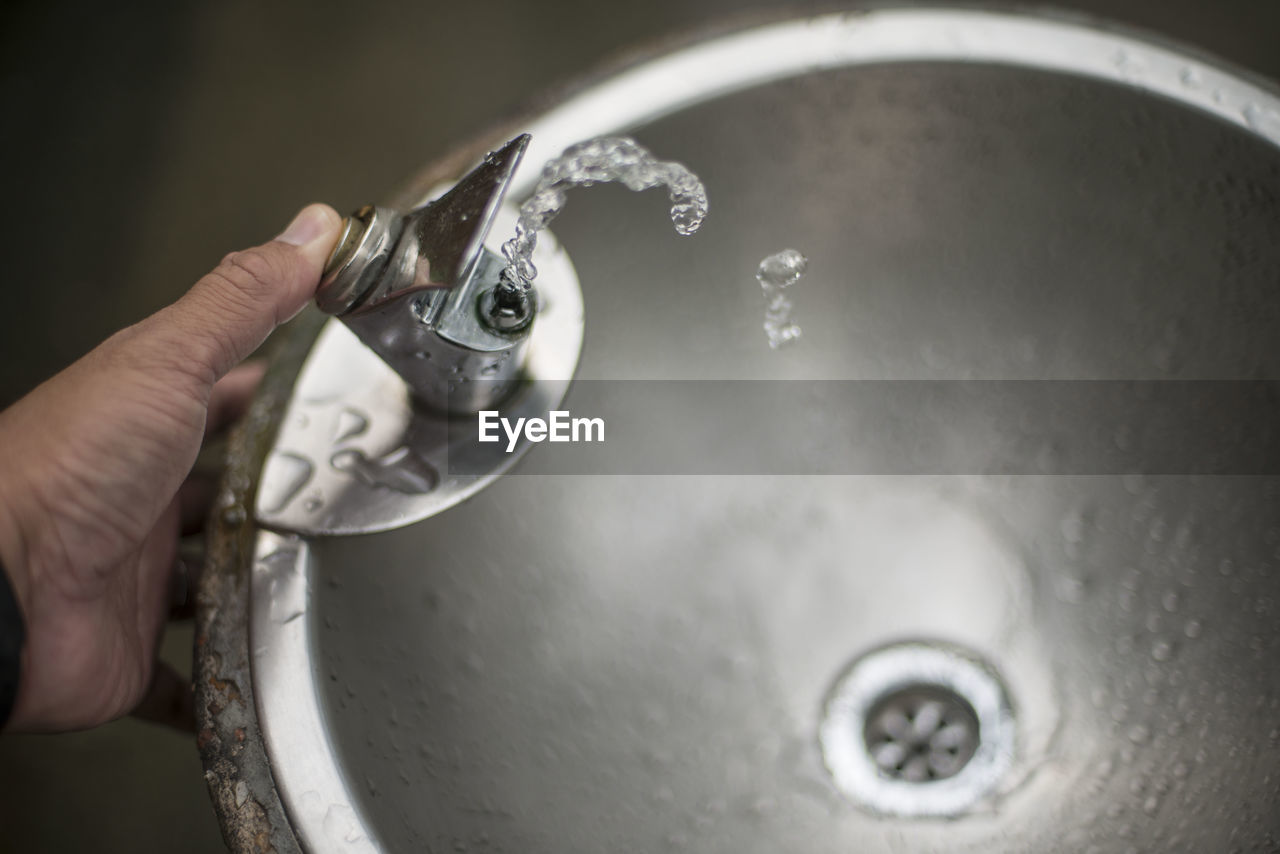 Cropped hand pressing faucet button of drinking fountain