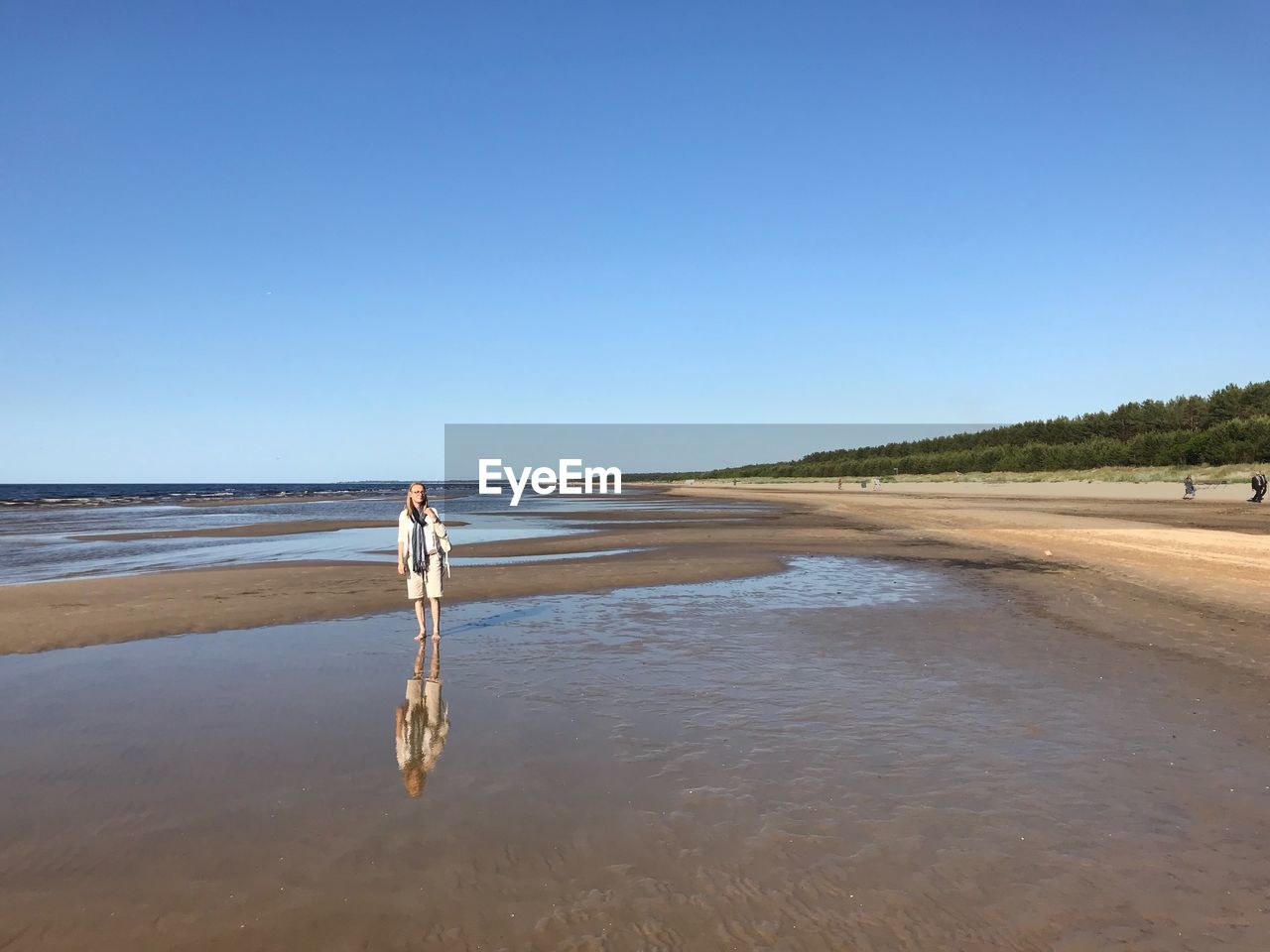 Mature woman standing at beach against clear blue sky