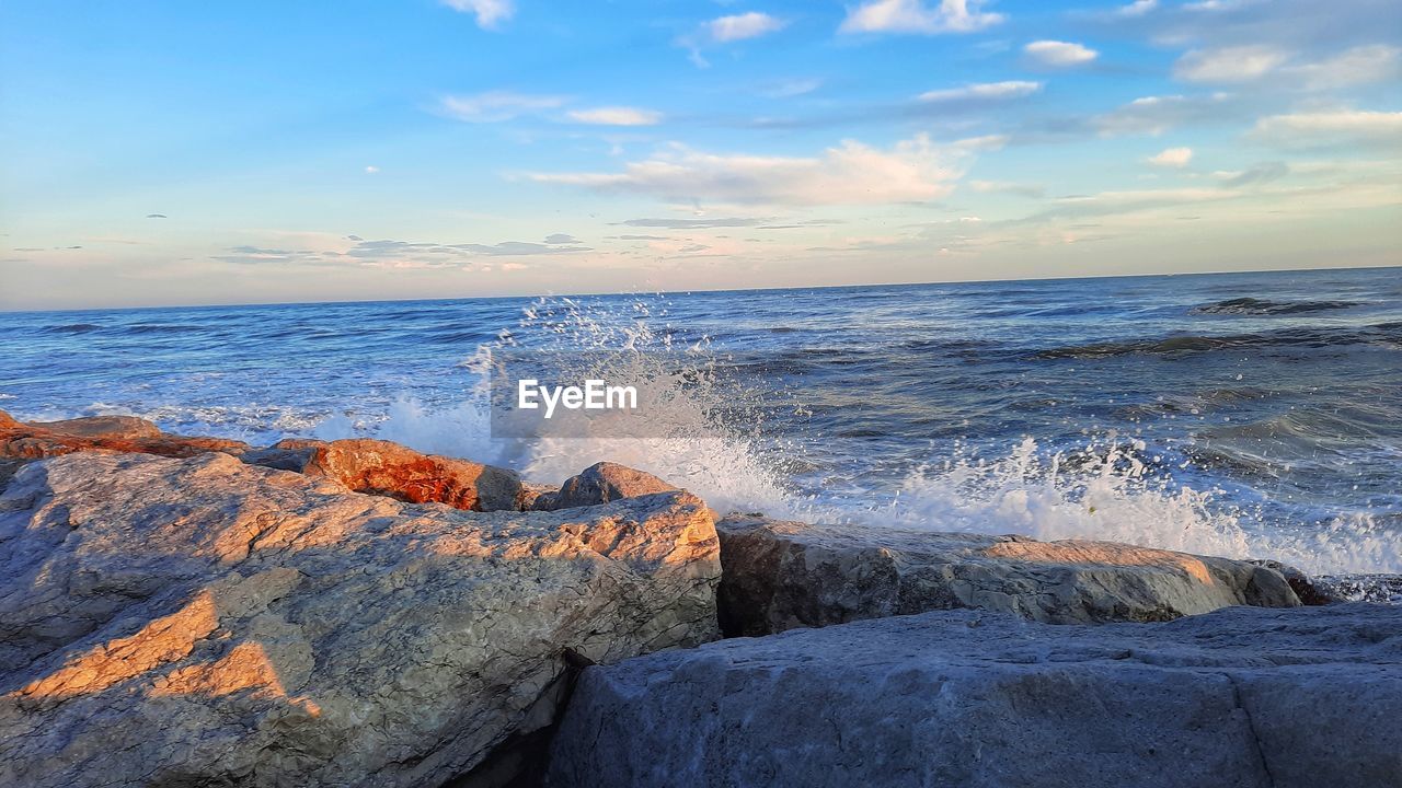sea, water, shore, rock, sky, ocean, body of water, wave, land, horizon, beach, motion, beauty in nature, wind wave, coast, horizon over water, scenics - nature, nature, cliff, cloud, sunrise, terrain, sports, water sports, no people, sand, blue, seascape, outdoors, breaking, splashing, morning, vacation, travel destinations, environment, power in nature, tranquility, idyllic, coastline, tranquil scene