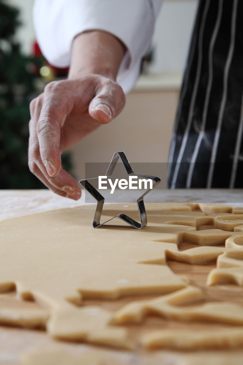 Cropped hands of chef cutting dough with pastry cutter at table