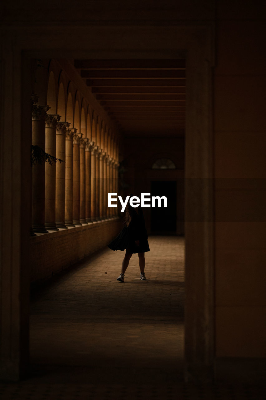 Full length of young woman standing in dark corridor