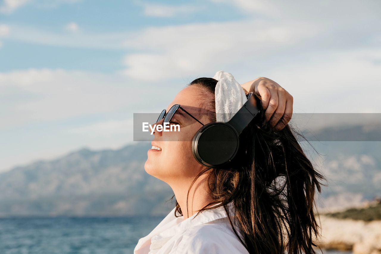 Side view of young woman in white shirt listening to music on headphones. summer, beach, lifestyle.