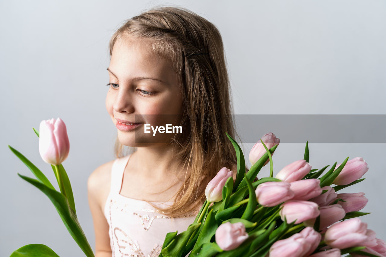 PORTRAIT OF SMILING WOMAN WITH PINK TULIPS AGAINST GRAY BACKGROUND