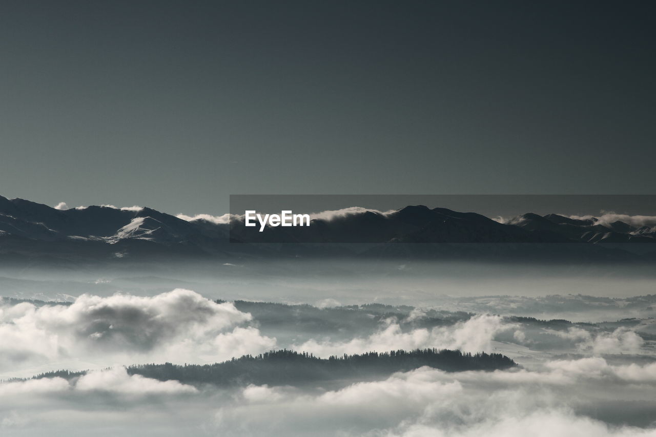 Scenic view of cloud covered mountains against clear sky at dusk