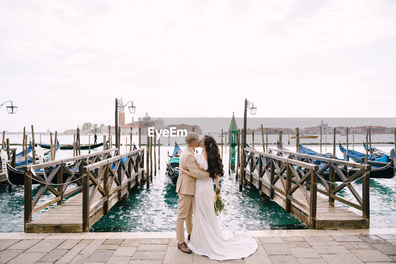 REAR VIEW OF WOMAN STANDING ON PIER AGAINST SKY