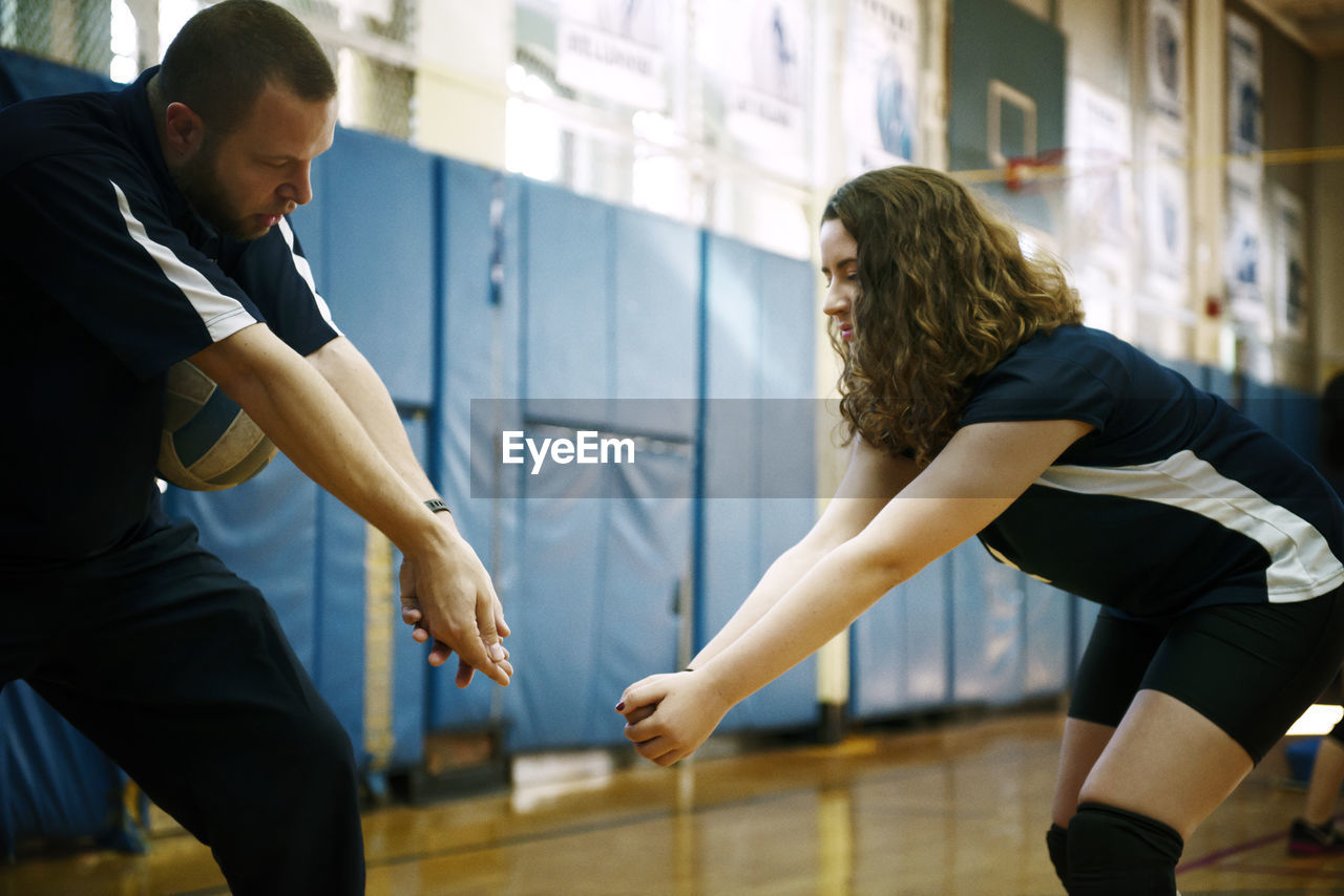 Coach teaching volleyball to teenage girl in court