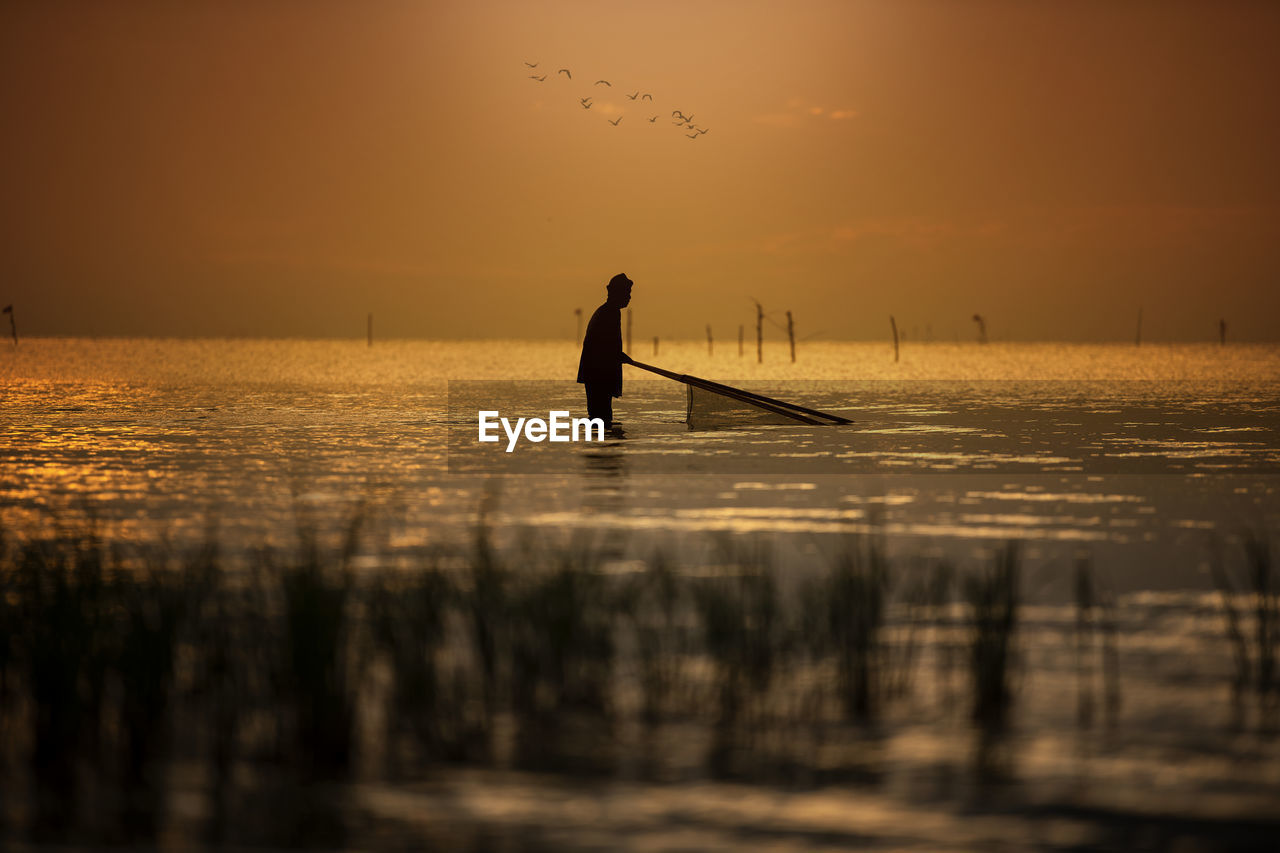 Silhouette man fishing in sea against sky during sunset