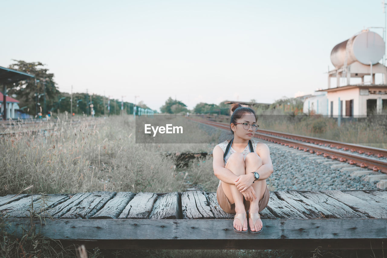 Thoughtful young woman sitting on boardwalk by railroad tracks