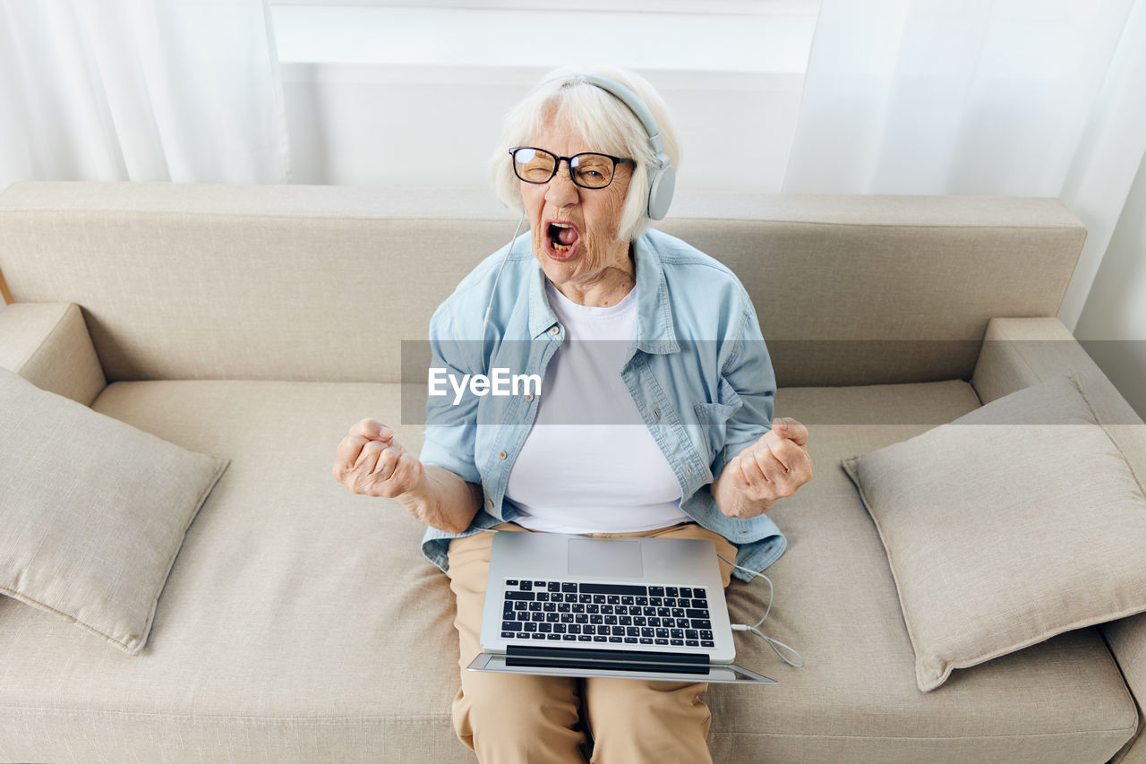 portrait of young woman using digital tablet while sitting on sofa at home