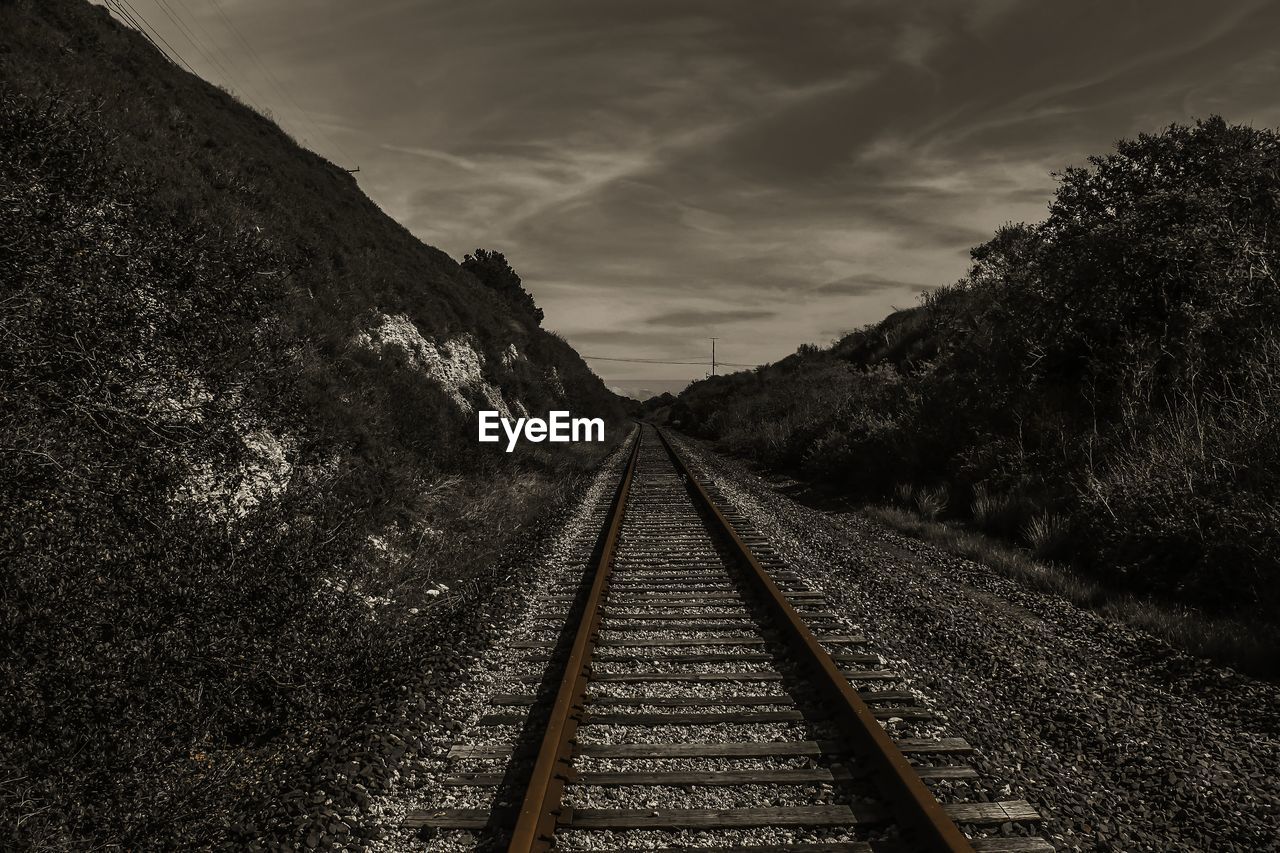 track, railroad track, rail transportation, darkness, transportation, sky, the way forward, nature, vanishing point, black and white, no people, monochrome, diminishing perspective, plant, cloud, black, tree, monochrome photography, morning, outdoors, mode of transportation, mountain, environment, line, railway, travel, sunlight, land, scenics - nature, horizon