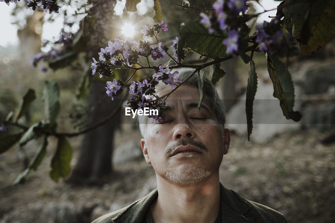 Mature man with eyes closed below blossoming tree in garden