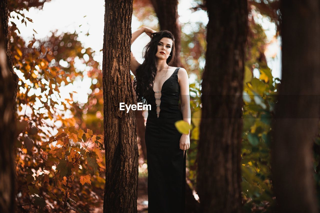 Portrait of woman standing by tree at forest