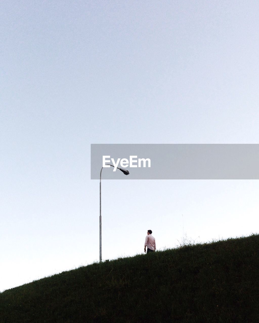 Low angle view of man walking on hill against clear sky during sunset